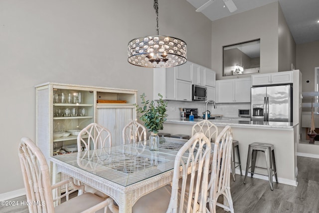 dining room with ceiling fan with notable chandelier, light hardwood / wood-style floors, and high vaulted ceiling