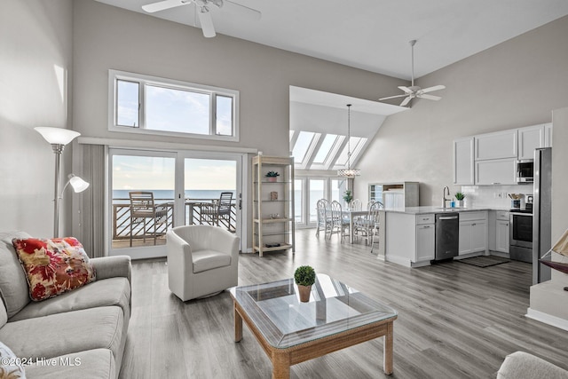 living room featuring a water view, high vaulted ceiling, ceiling fan with notable chandelier, and light wood-type flooring