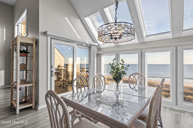 dining area featuring lofted ceiling, a water view, an inviting chandelier, and light hardwood / wood-style floors