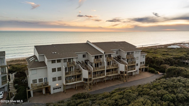 aerial view at dusk featuring a water view and a view of the beach