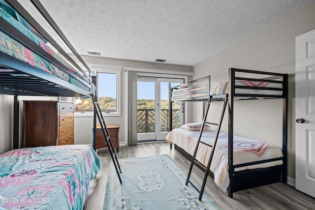 bedroom with access to exterior, hardwood / wood-style floors, and a textured ceiling