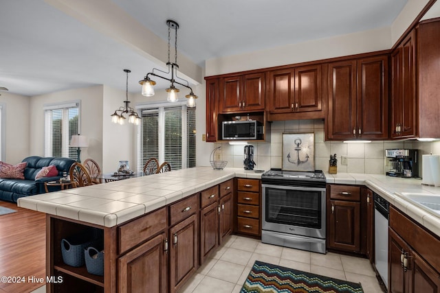 kitchen featuring kitchen peninsula, appliances with stainless steel finishes, decorative backsplash, decorative light fixtures, and tile counters