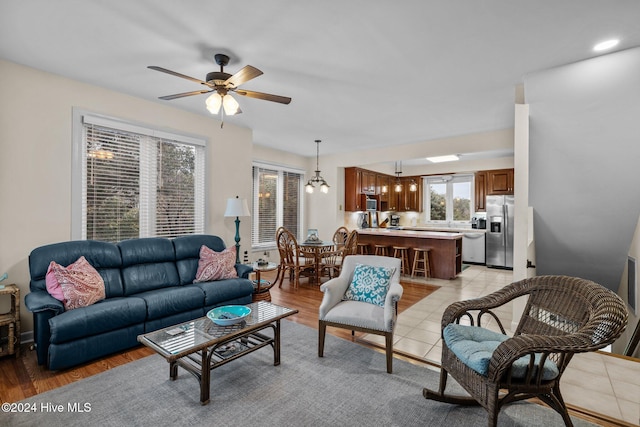 living room featuring ceiling fan with notable chandelier and light hardwood / wood-style flooring