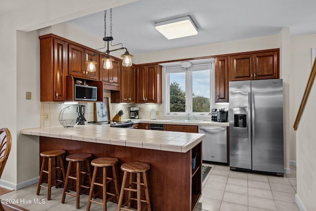 kitchen with backsplash, kitchen peninsula, tile countertops, and appliances with stainless steel finishes