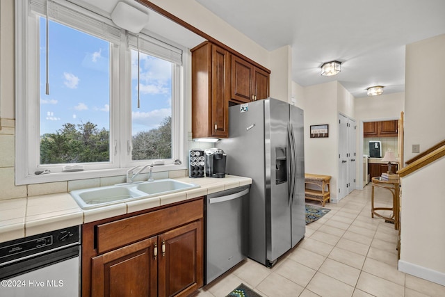 kitchen featuring tile countertops, sink, light tile patterned flooring, and stainless steel appliances