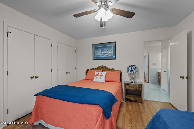 bedroom with hardwood / wood-style flooring, ceiling fan, and two closets