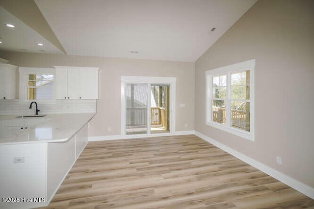 interior space featuring a sink, light countertops, vaulted ceiling, white cabinetry, and light wood-type flooring