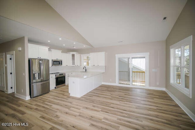 kitchen with high vaulted ceiling, a sink, white cabinetry, appliances with stainless steel finishes, and a peninsula