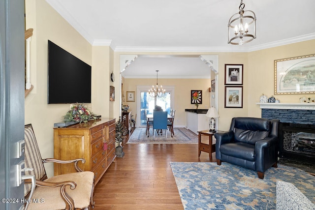 living room with hardwood / wood-style floors, an inviting chandelier, ornamental molding, and a stone fireplace