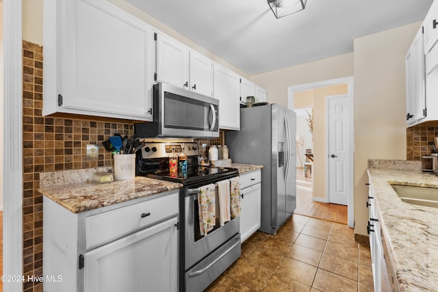 kitchen with white cabinets, stainless steel appliances, light stone counters, and tasteful backsplash