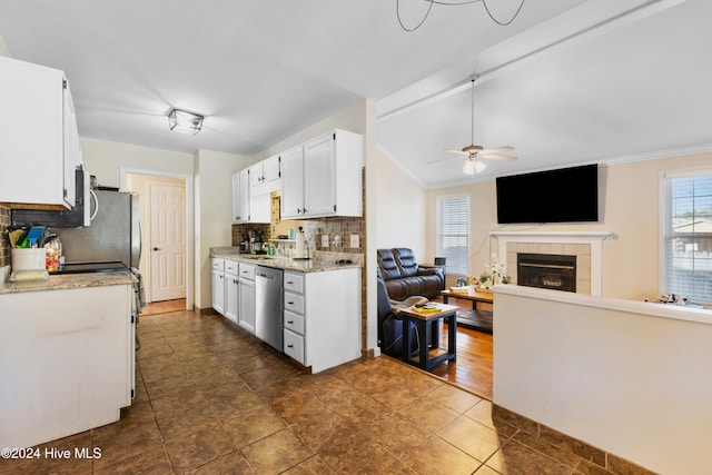 kitchen featuring backsplash, white cabinets, ceiling fan, dishwasher, and a tiled fireplace