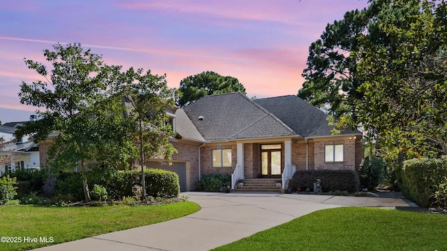 view of front of property featuring brick siding, driveway, a front lawn, and roof with shingles
