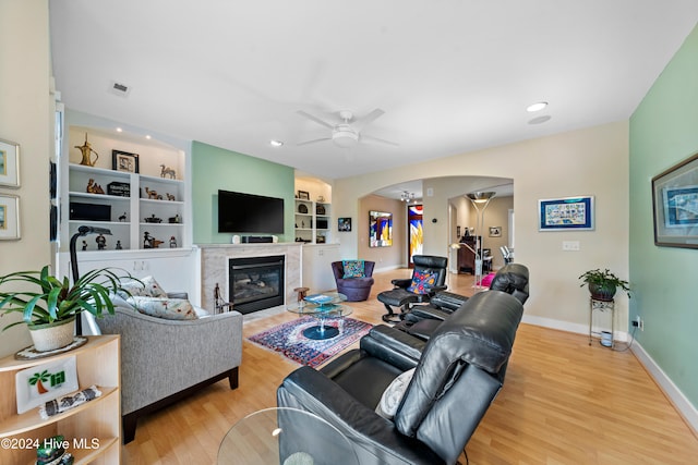 living room featuring ceiling fan, light hardwood / wood-style floors, and built in shelves