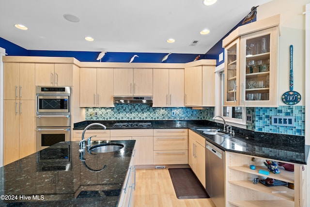 kitchen with light brown cabinetry, stainless steel appliances, dark stone counters, and sink