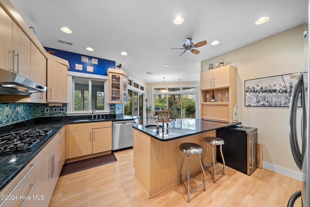 kitchen with light brown cabinets, appliances with stainless steel finishes, a ceiling fan, and a breakfast bar area