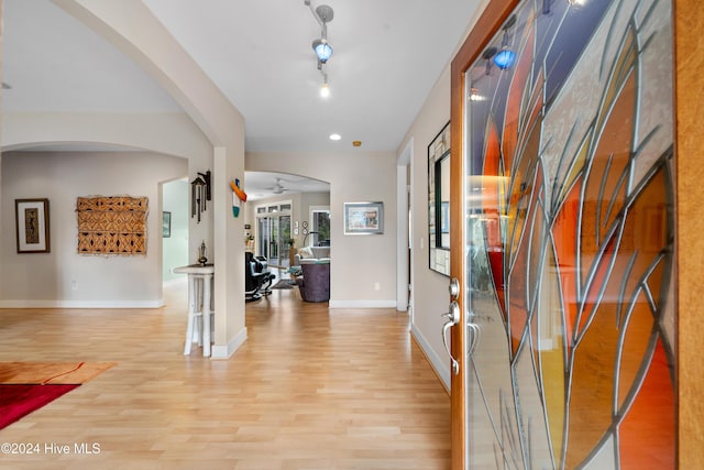 hallway featuring arched walkways, light wood-style flooring, and baseboards