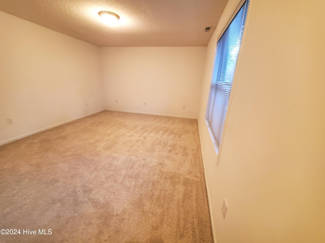 empty room with light colored carpet and a textured ceiling