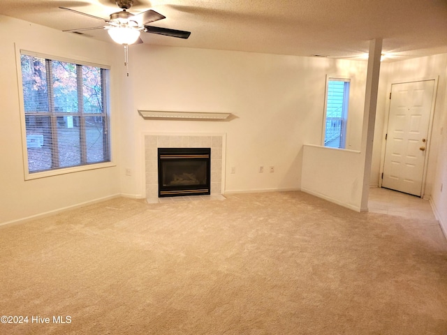 unfurnished living room with a textured ceiling, ceiling fan, a fireplace, and light carpet