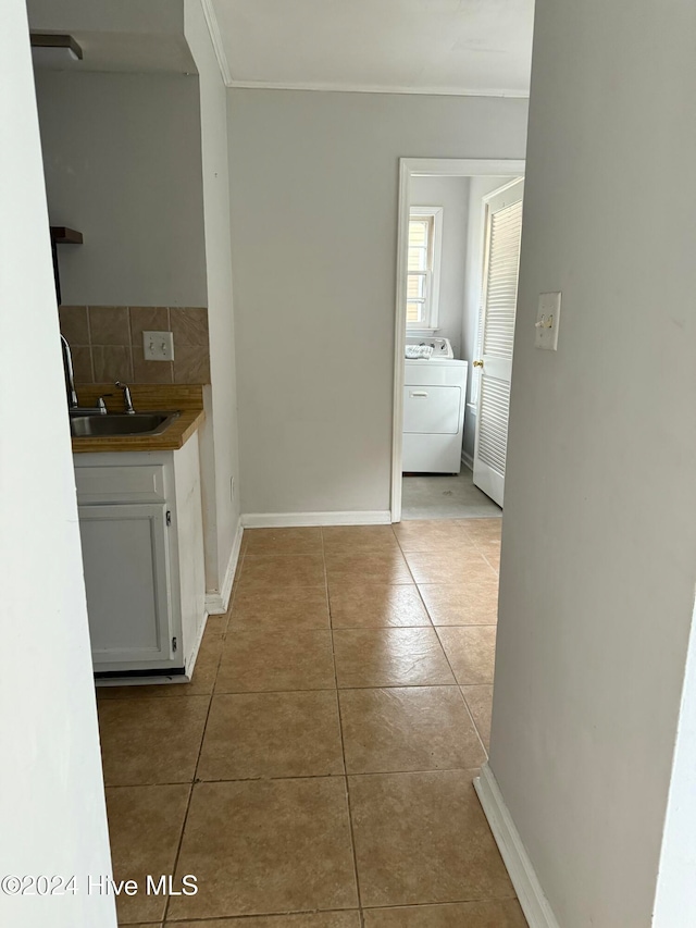 hallway featuring washer / clothes dryer, sink, light tile patterned flooring, and ornamental molding