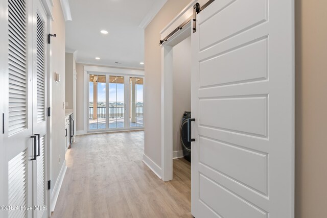 hallway with a barn door, crown molding, washer / clothes dryer, and light wood-type flooring