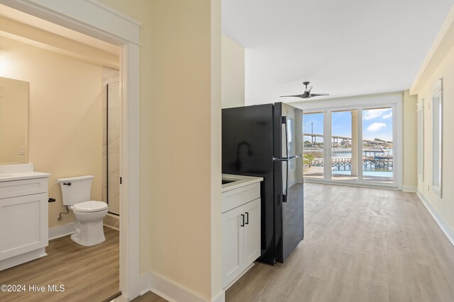 kitchen with ceiling fan, black fridge, white cabinetry, and light wood-type flooring