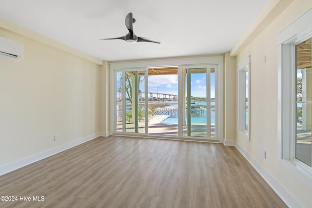 empty room featuring light wood-type flooring, a water view, a wall unit AC, and ceiling fan