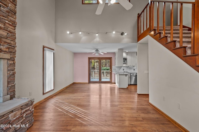 unfurnished living room with a towering ceiling, light hardwood / wood-style floors, a stone fireplace, and ceiling fan