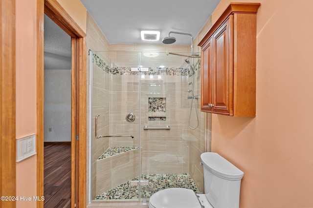 bathroom with hardwood / wood-style flooring, toilet, and a shower with shower door