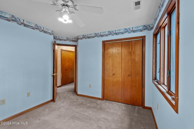 unfurnished bedroom with ceiling fan, a closet, light colored carpet, and a textured ceiling