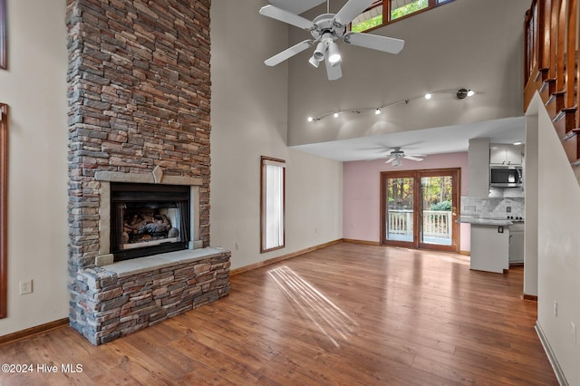 unfurnished living room with a fireplace, a towering ceiling, light hardwood / wood-style flooring, and ceiling fan