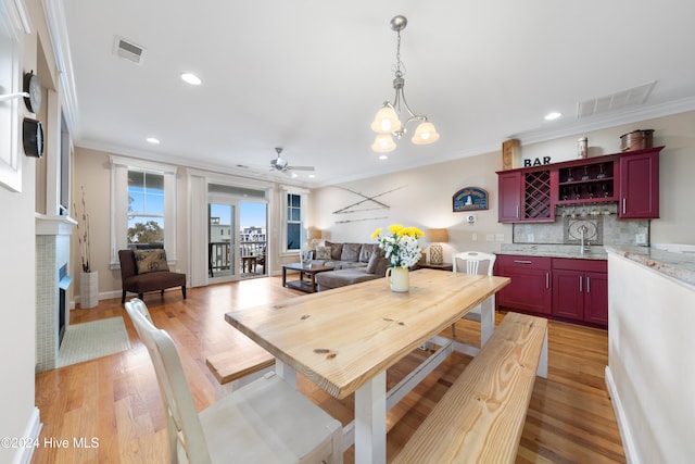 dining space featuring sink, ornamental molding, ceiling fan with notable chandelier, and light wood-type flooring