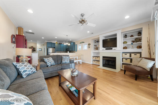 living room featuring ceiling fan with notable chandelier, light wood-type flooring, and crown molding