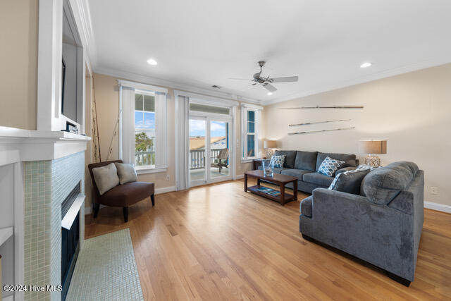 living room featuring light wood-type flooring, ceiling fan, crown molding, and a tiled fireplace