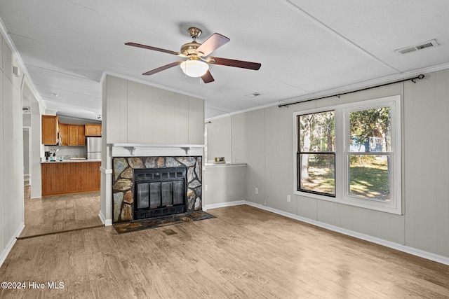 living room with ceiling fan, a stone fireplace, light hardwood / wood-style flooring, wood walls, and a textured ceiling