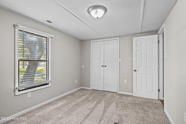 unfurnished bedroom with carpet, a textured ceiling, wooden walls, and a closet