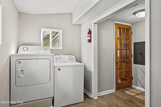 clothes washing area featuring a textured ceiling, electric panel, washer and clothes dryer, and dark wood-type flooring