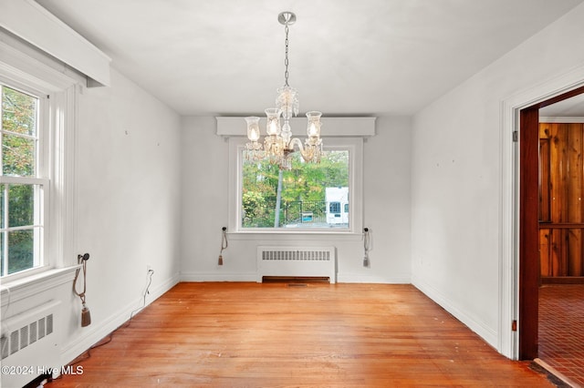 unfurnished dining area with radiator, light hardwood / wood-style flooring, and a notable chandelier