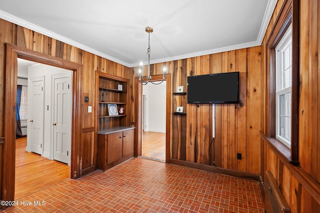 unfurnished dining area with wooden walls, built in features, an inviting chandelier, and ornamental molding