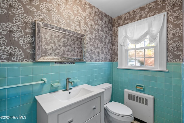 bathroom with vanity, toilet, radiator, and tile walls