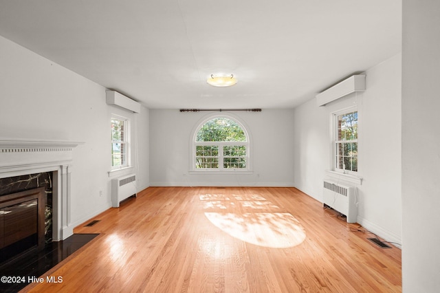 unfurnished living room with radiator heating unit, light hardwood / wood-style floors, and a wall mounted AC