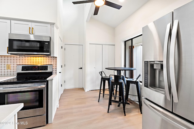 kitchen with appliances with stainless steel finishes, tasteful backsplash, white cabinets, light hardwood / wood-style floors, and lofted ceiling