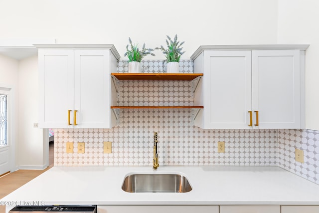 kitchen with decorative backsplash, white cabinetry, sink, and light wood-type flooring