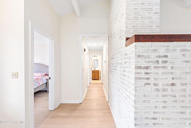 hall with beamed ceiling, brick wall, and light hardwood / wood-style flooring