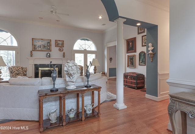 living room with a healthy amount of sunlight, light wood-type flooring, crown molding, and ornate columns