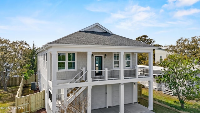 1514 Mackerel Ln, Carolina Beach, NC 28428 - coastal inspired home with central air condition unit, covered porch, an attached garage, fence, and roof with shingles