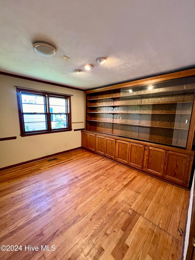 empty room with light wood-type flooring, a textured ceiling, and ornamental molding