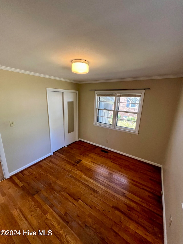 unfurnished bedroom featuring dark hardwood / wood-style flooring, ornamental molding, and a closet