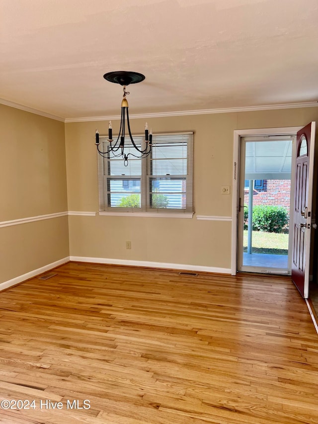 unfurnished dining area featuring light wood-type flooring, ornamental molding, and an inviting chandelier