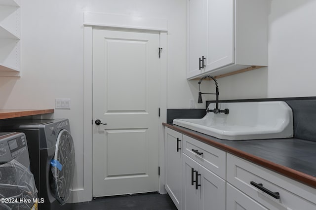 clothes washing area featuring dark hardwood / wood-style flooring, washer and clothes dryer, cabinets, and sink