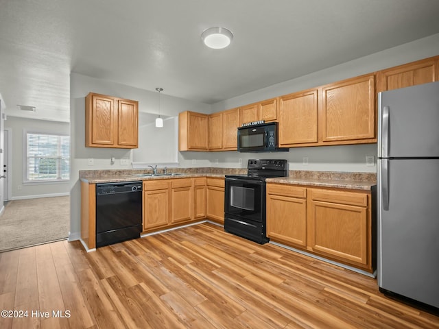 kitchen featuring sink, black appliances, decorative light fixtures, and light wood-type flooring